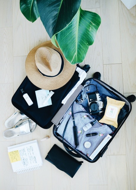 Opened suitcase with sun hat, camera, sandles